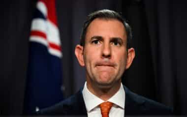 Australian Treasurer Jim Chalmers stands in front of a national flag during a government press conference