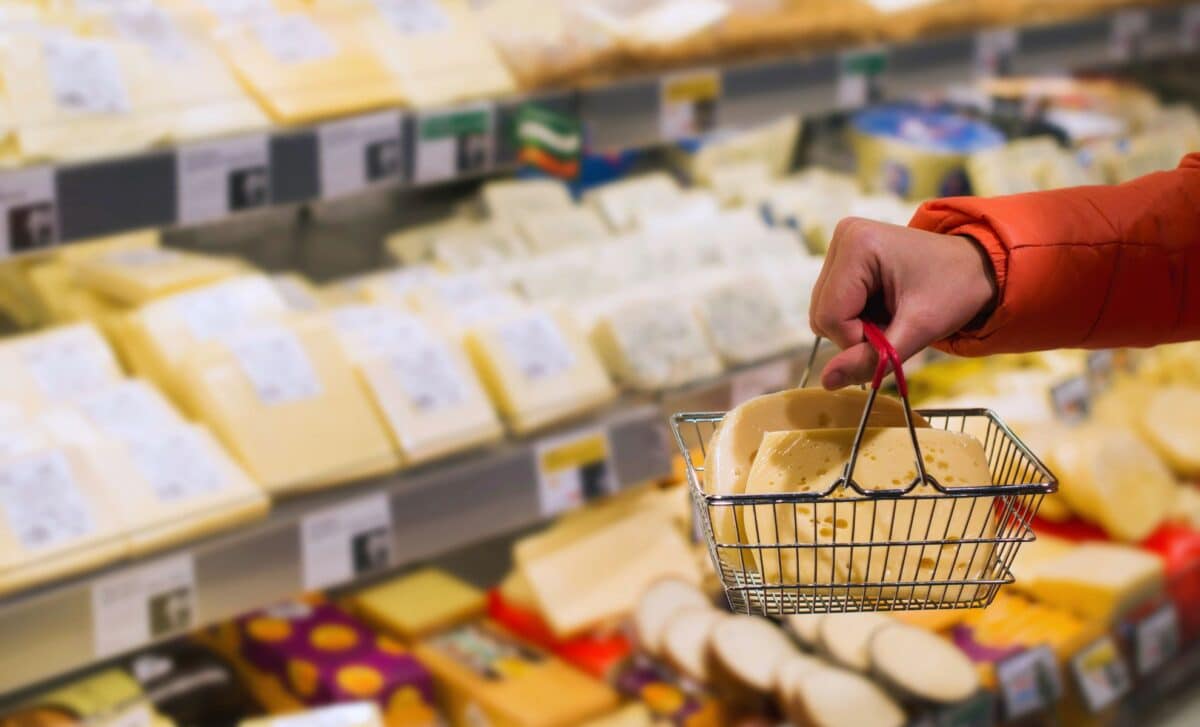 Hand holding a small shopping basket filled with cheese at a supermarket