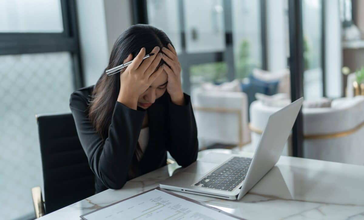 A Stressed Woman Holding Her Head at a Desk.