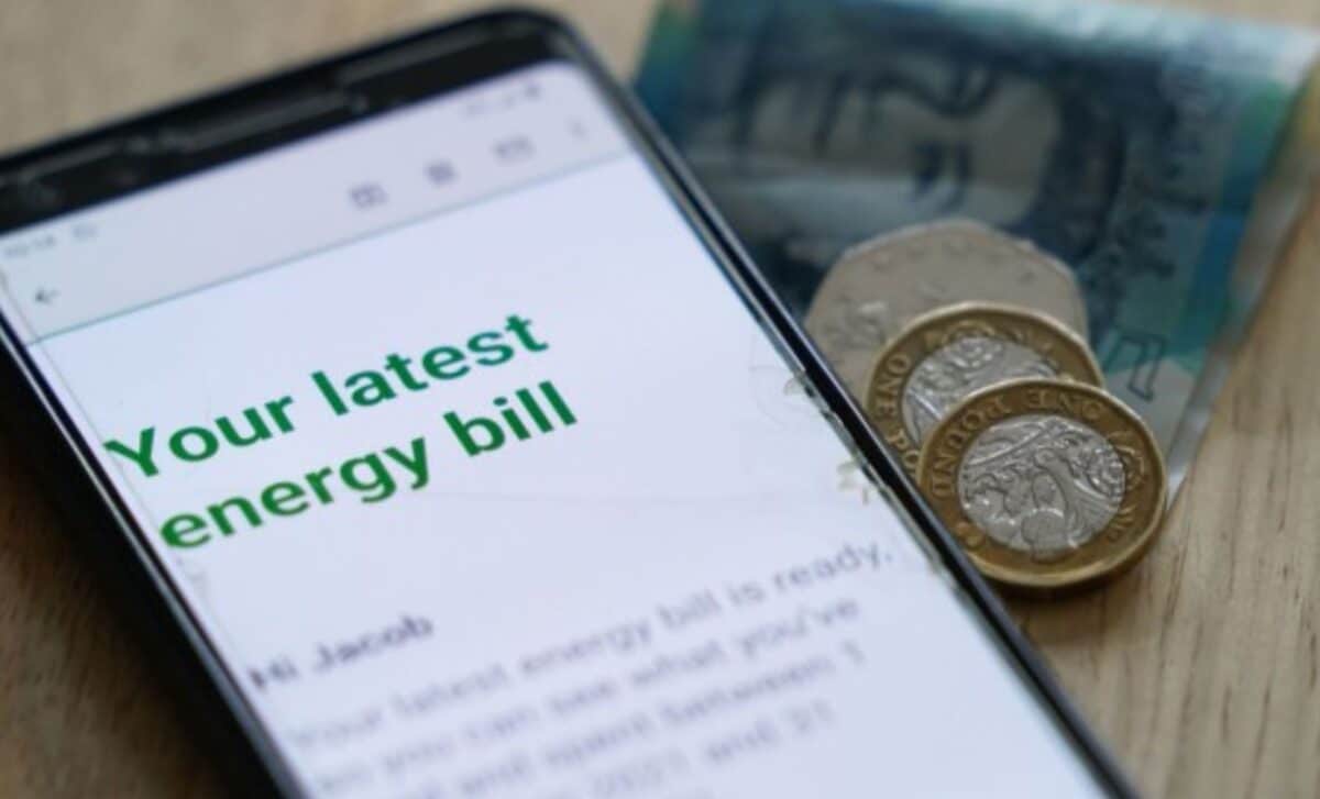 Phone Screen Displaying Energy Bill with UK Bank Note and Coins Besides it to refer to the rising energy price cap