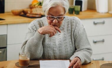 Old Lady Wearing Glasses Reading A DWP Document With Cup Of Coffee Besides Her