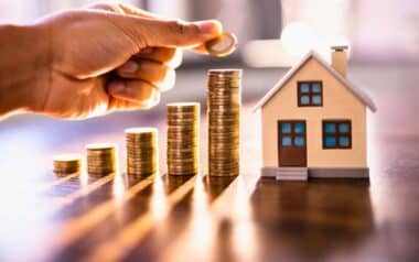 Homeowners-A hand placing a coin on top of a stack of coins, symbolizing growth