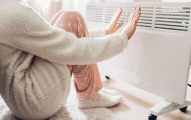 Households-person sitting close to a portable heater, with hands stretched out to feel the warmth