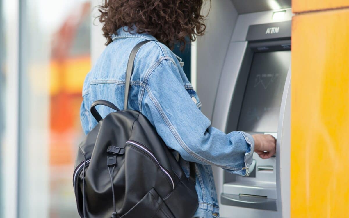 a person withdrawing cash from an ATM, focusing on their hand retrieving a stack of money