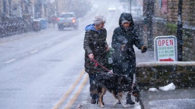 England-two individuals walking on a snow-covered street, accompanied by a dog