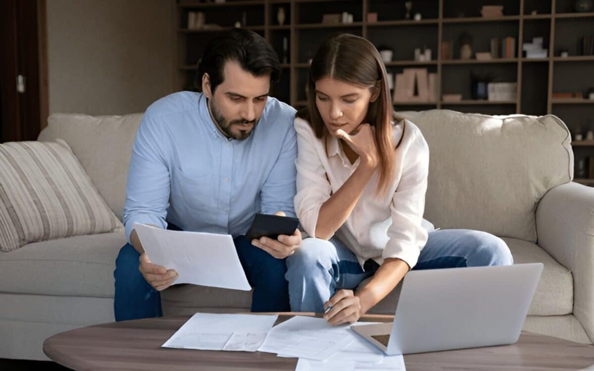 Families-couple sitting closely together on a sofa, deeply focused on managing household finances or planning