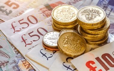 Households-British currency, including £50 and £10 banknotes alongside stacks of one-pound coins and other smaller coins.