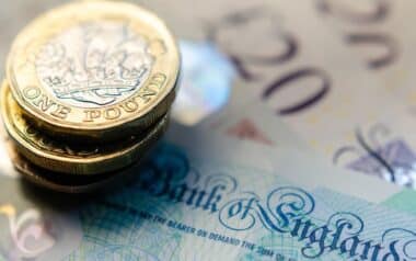 UK-close-up of stacked one-pound coins placed against a blurred backdrop of British banknotes.