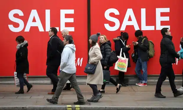 Retailers-bustling street scene in front of a retail store with large red sale banners prominently displaying the word SALE