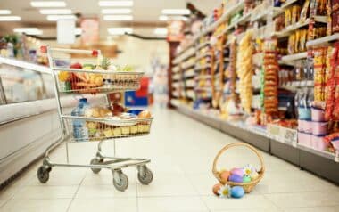 A supermarket aisle with a cart of groceries and a basket of colourful Easter eggs.