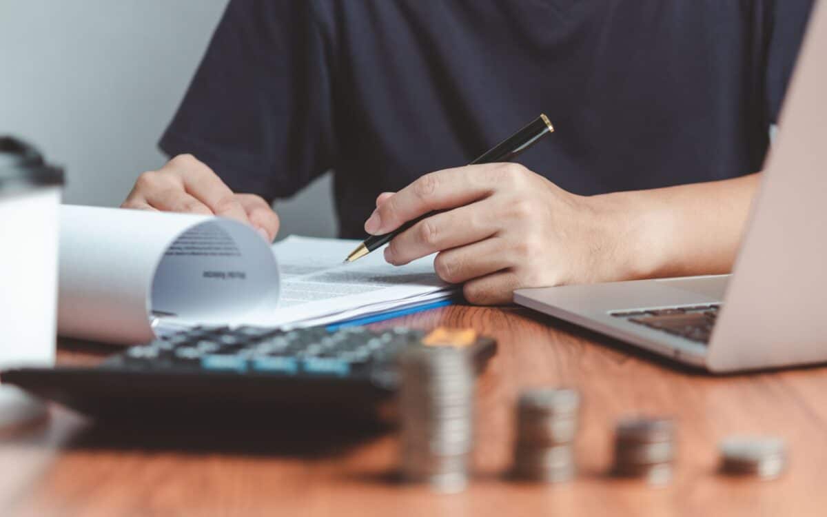 A person reviews financial documents at a desk with a laptop