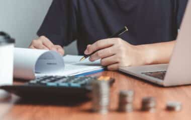 A person reviews financial documents at a desk with a laptop