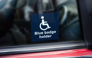A sticker displaying "Blue Badge holder" is visible on a car window, indicating that the vehicle is used by or for someone with a Blue Badge permit for disabled parking.