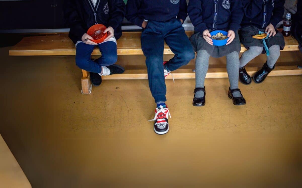 Children sit on a bench during lunch, highlighting the daily impact of the Two-Child Benefit Cap on family life