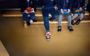 Children sit on a bench during lunch, highlighting the daily impact of the Two-Child Benefit Cap on family life