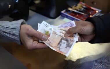 A person handing over £10 and £20 banknotes, likely as part of a transaction