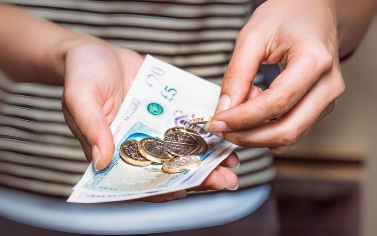 A person holding a handful of coins and banknotes in British currency