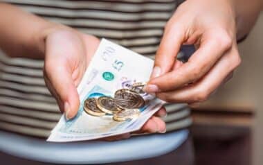 A person holding a handful of coins and banknotes in British currency