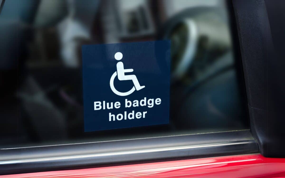 A Blue Badge holder sticker is displayed on a car window