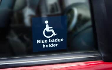 A Blue Badge holder sticker is displayed on a car window