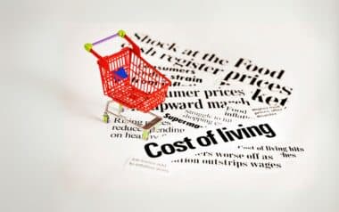 Miniature shopping cart on headlines concerning cost of living