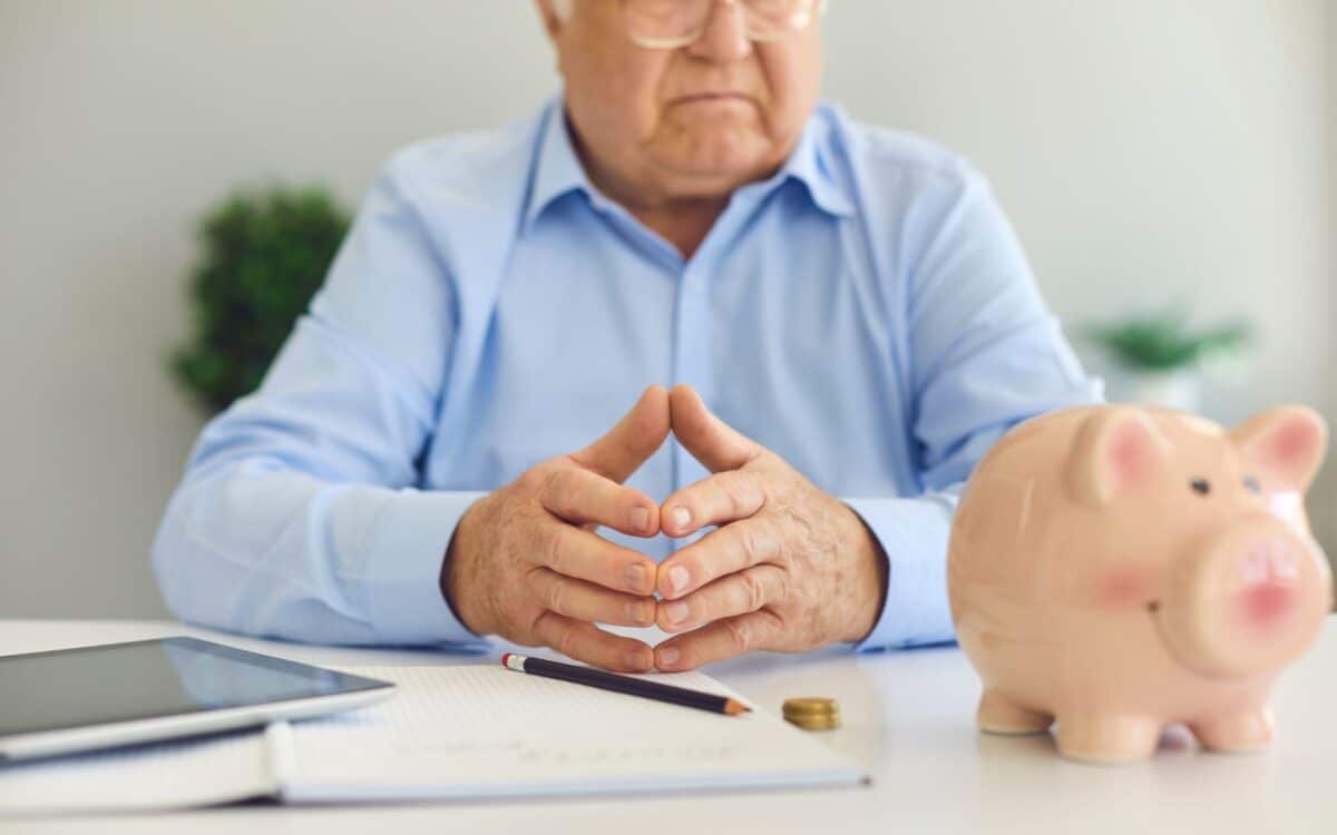 Senior Man at Desk with Notebook, Tablet and Piggy Bank Managing Personal Finance