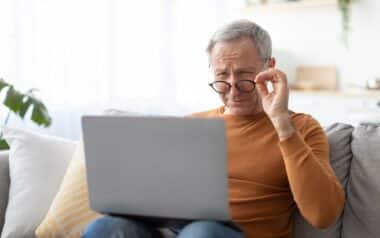 Mature man squinting using laptop, looking at screen