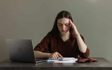 Upset Woman Using Calculator at Grey Table. Financial Problems