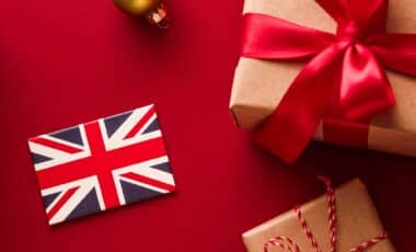 A festive flat-lay displaying two brown-paper gifts, a Union Jack flag, and a gold ornament against a deep red background.
