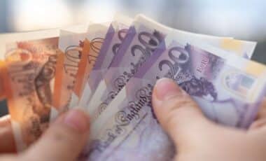 A man's hand holding British pound banknotes.