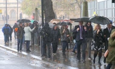 Group of people seen walking on the sidewalk with umbrellas during heavy rain, London, UK.