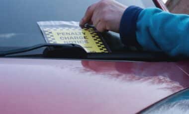 A hand pulling a yellow parking ticket out from under a vehicle's wiper blade.
