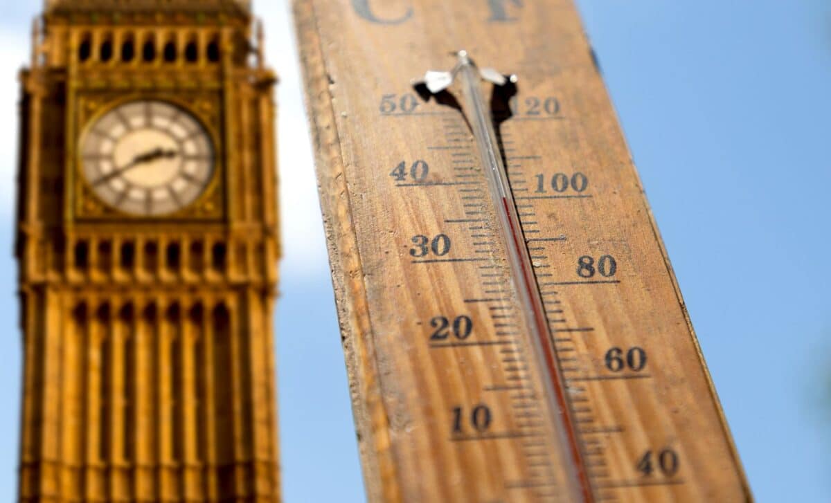 A wooden outdoor thermometer showing a high temperature of around 40°C (104°F) with Big Ben blurred in the background under a clear blue sky.