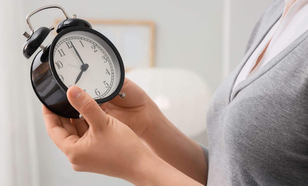 Woman setting the time on her alarm clock in her bedroom, close-up.