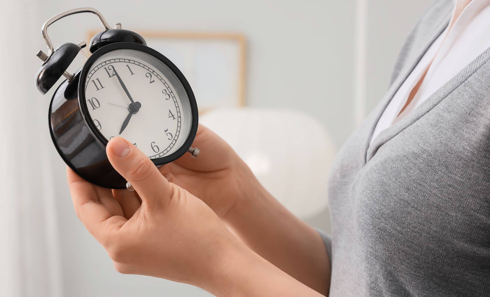 Woman setting the time on her alarm clock in her bedroom, close-up.