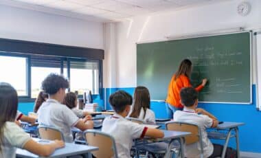 Teacher writing on chalkboard teaching students in classroom