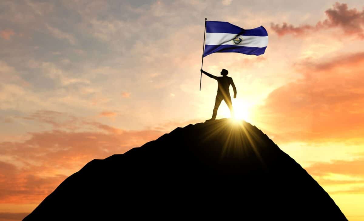 Flag of El Salvador raised by a human at the top of a mountain, by sunset