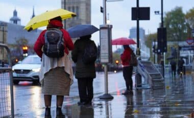 A Group Of People Holding Umbrellas While Standing On A Sidewalk, Likely During Rainy Weather