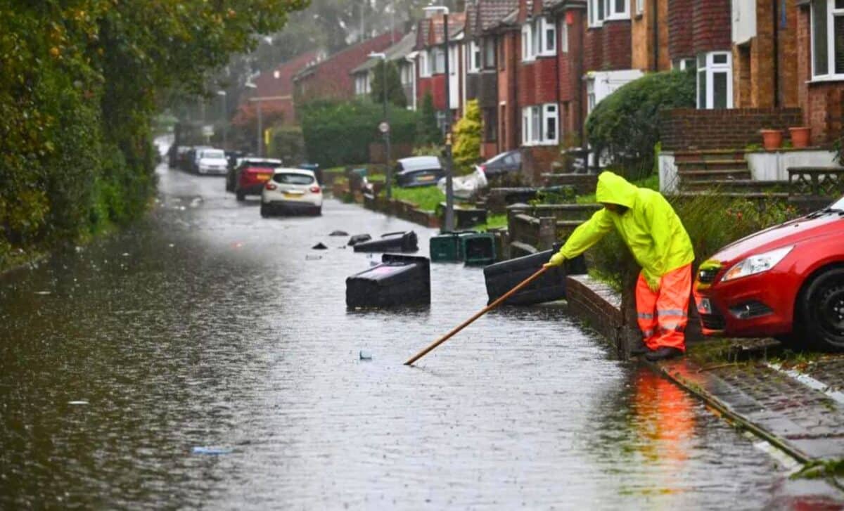 A Person In A Yellow Rain Suit Cleaning A Flooded Street.