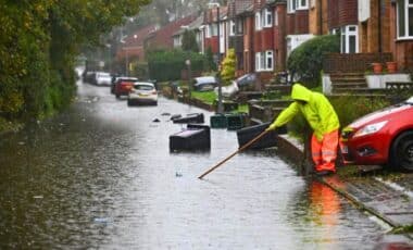 A Person In A Yellow Rain Suit Cleaning A Flooded Street.