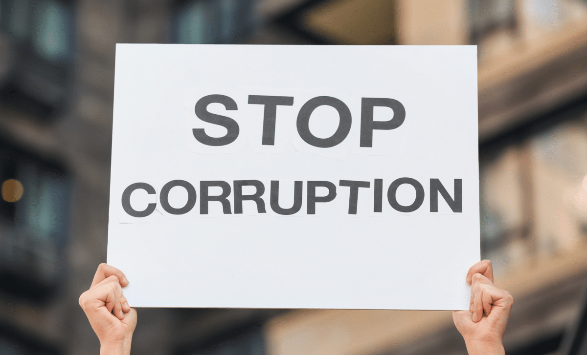 Hands Lifting White Sheet of Paper with " STOP Corruption" Written on It