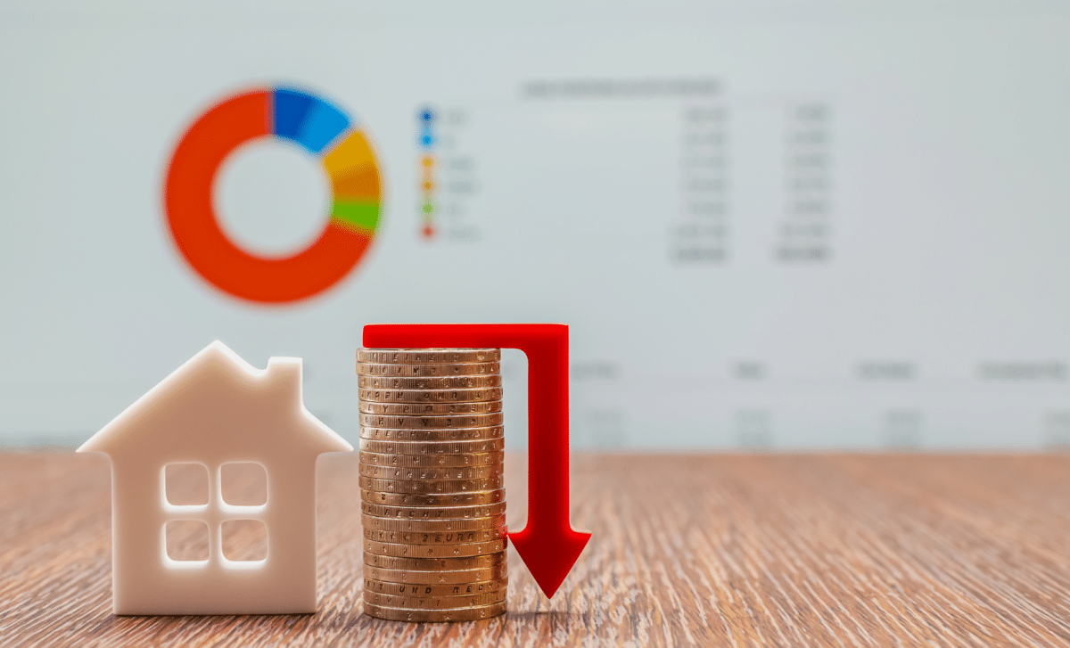 Tiny White House and Coins Besides it with Down Arrow Symbolizing UK House Price Decline Slowing