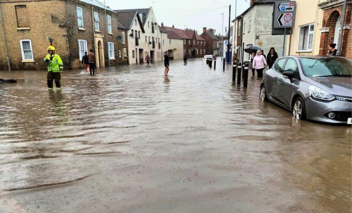 Weather, : A Flooded Street With People And Cars Navigating Through The Water