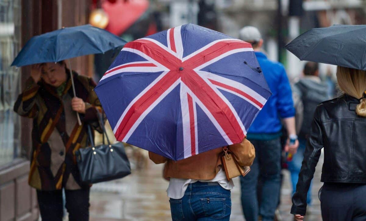 People Walking With Umbrellas On A Street In A Rainy Day.