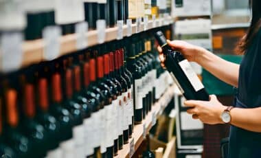 Woman Choosing A Bottle Of Red Wine From The Shelf In A Supermarket.