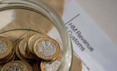 Jar Of Pound Coins On Top Of An Opened HMRC Tax Letter