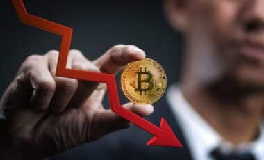 Man Holding Bitcoin Next To Decreasing Arrow