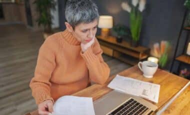 Woman In An Orange Sweater Sitting At A Desk With A Laptop And A Cup Of Coffee Nearby