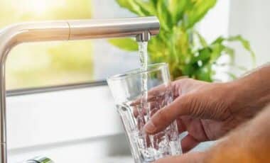 Hand Holding A Glass Under A Running Tap, Filling It With Water In A Kitchen Sink