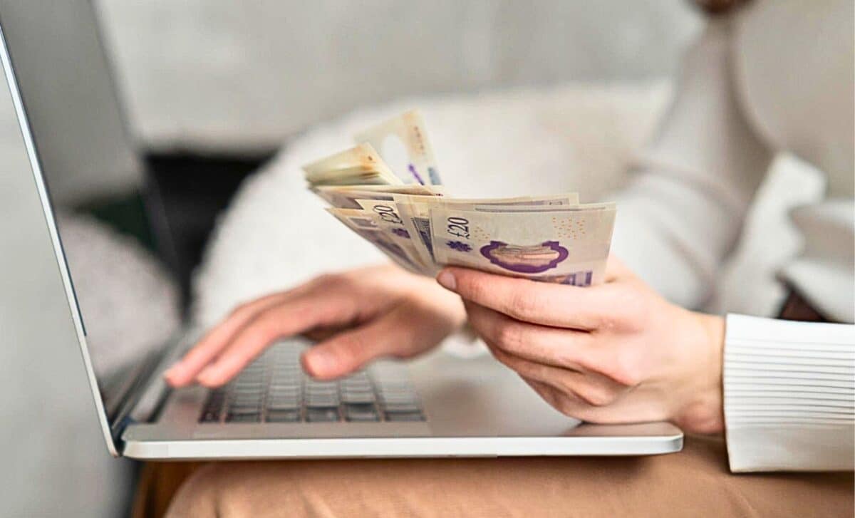 A Woman With A Handful Of Cash Payments In Front Of A Computer Screen